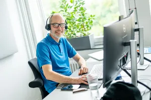 Ein Mitarbeiter mit Headset lächtelt in die Kamera